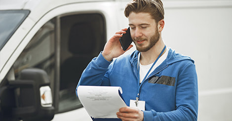 Delivery man talking to the phone while holding clipboard behind the van photo